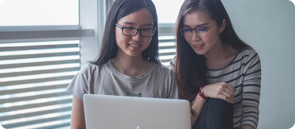 Two women collaborating and smiling while looking at a laptop